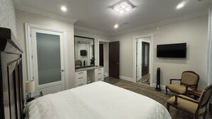 A bedroom with a large bed, a dresser, a mirror, a television, and a chair.