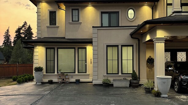 A modern two-story house with a driveway, potted plants, and a car parked in the garage.