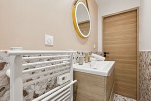 A bathroom with a white towel rack, a sink with a gold faucet, a mirror with a gold frame, and a wooden door.