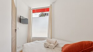 Ein Hotelzimmer mit einem Bett, einem an der Wand montierten Fernseher und einem Fenster mit Vorhängen.