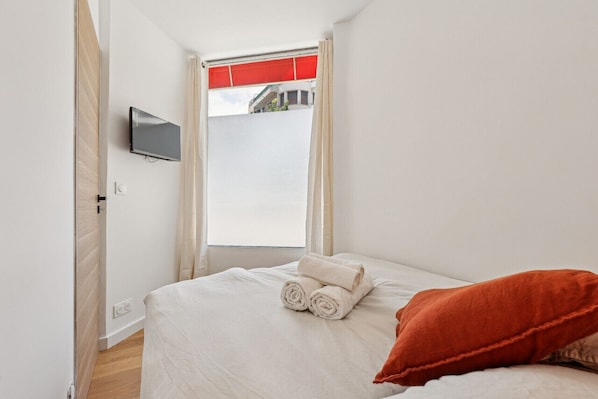 A hotel room with a bed, a TV mounted on the wall, and a window with curtains.