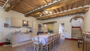 Una cocina con vigas de madera, una mesa de comedor con sillas y una escalera que sube a un nivel superior.