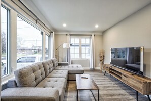 A modern living room with a sectional sofa, a flat-screen TV, and a wooden coffee table. - Newly Relax Inn Walk to Falls U1 (Niagara Falls)