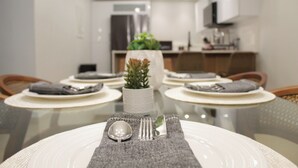 Mesa de comedor preparada para cuatro, con platos blancos, cubiertos y un posavasos gris.