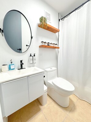 A modern bathroom with a white sink, mirror, and toilet. There are wooden shelves above the toilet with toiletries. - Aqua Dream Hideaway at Aquatika Beach Villas (Loiza)