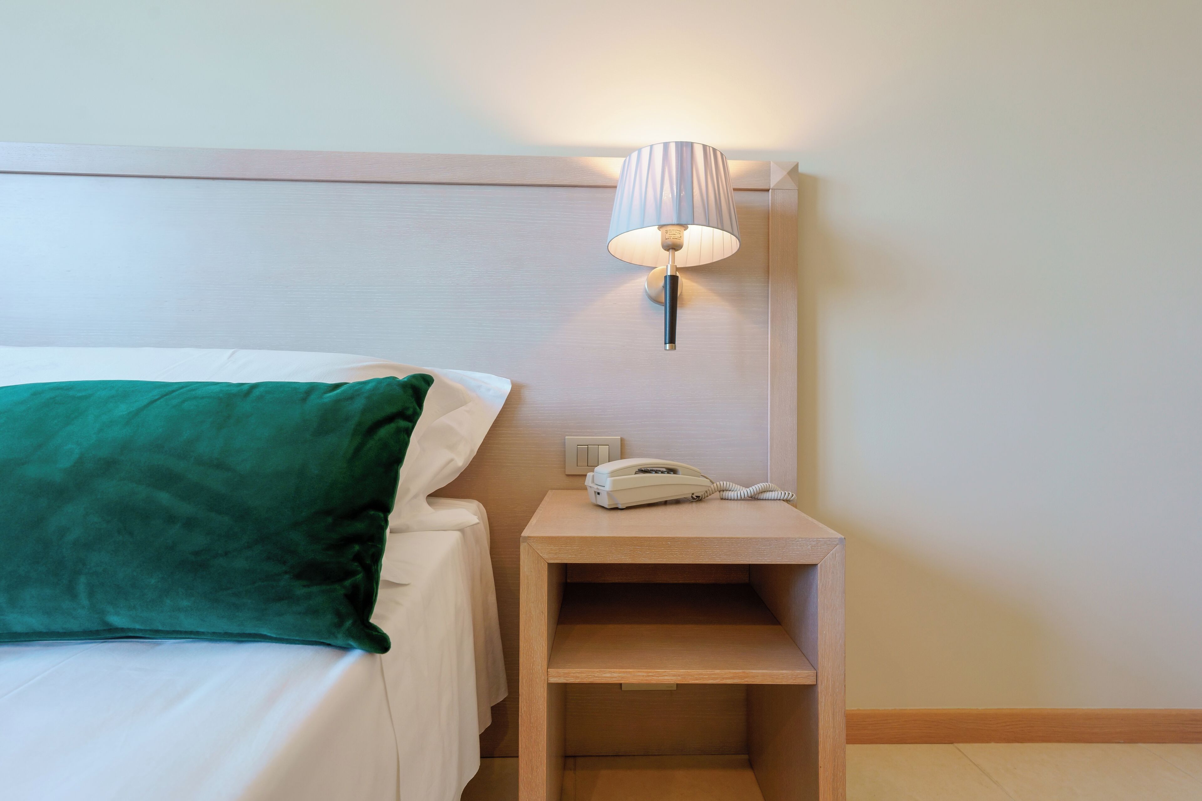 A neatly made bed with a green pillow, a bedside table with a lamp, and a phone.