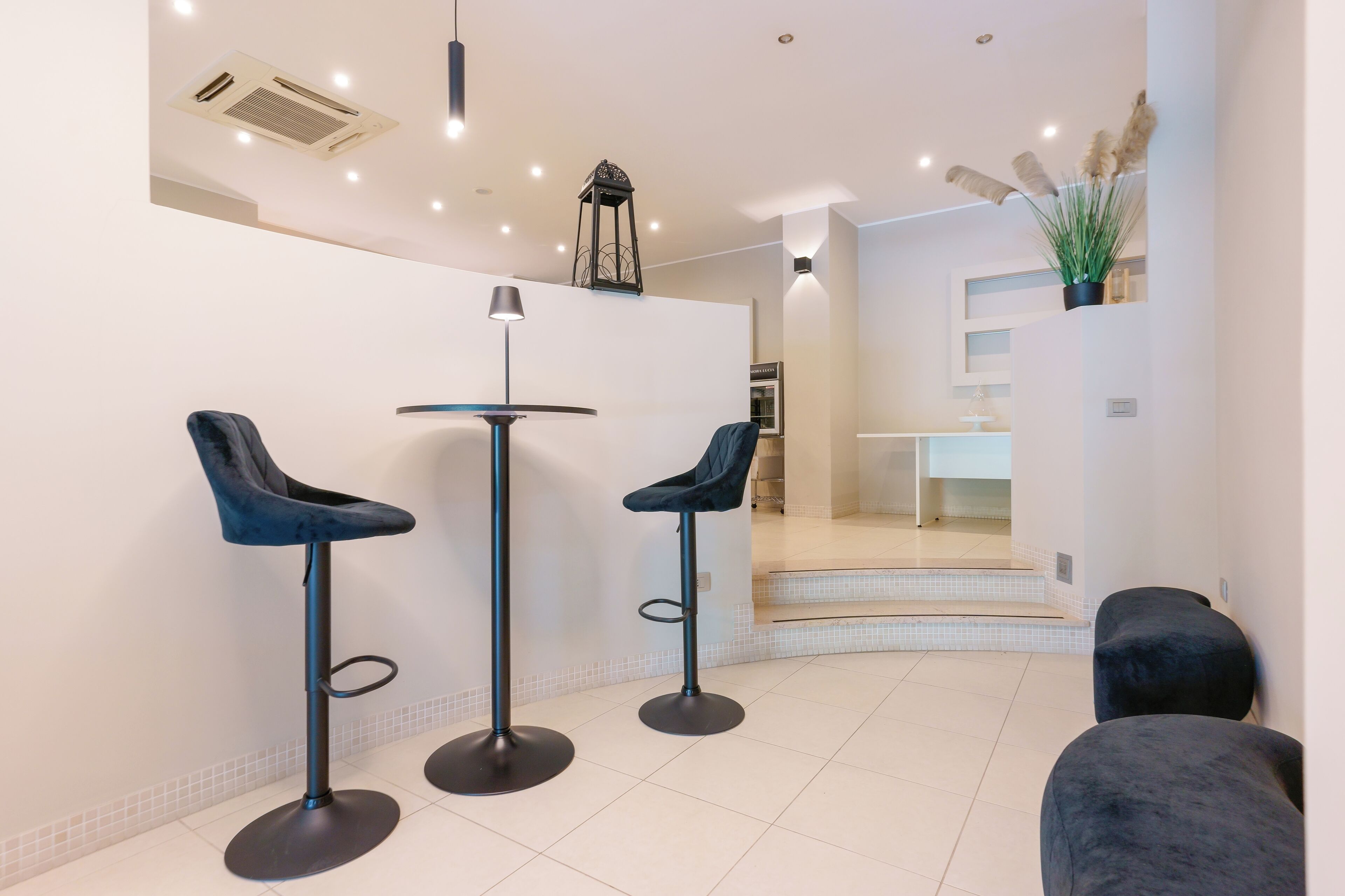 A modern interior with three dark blue bar stools, a floor lamp, and a staircase leading to a second level.