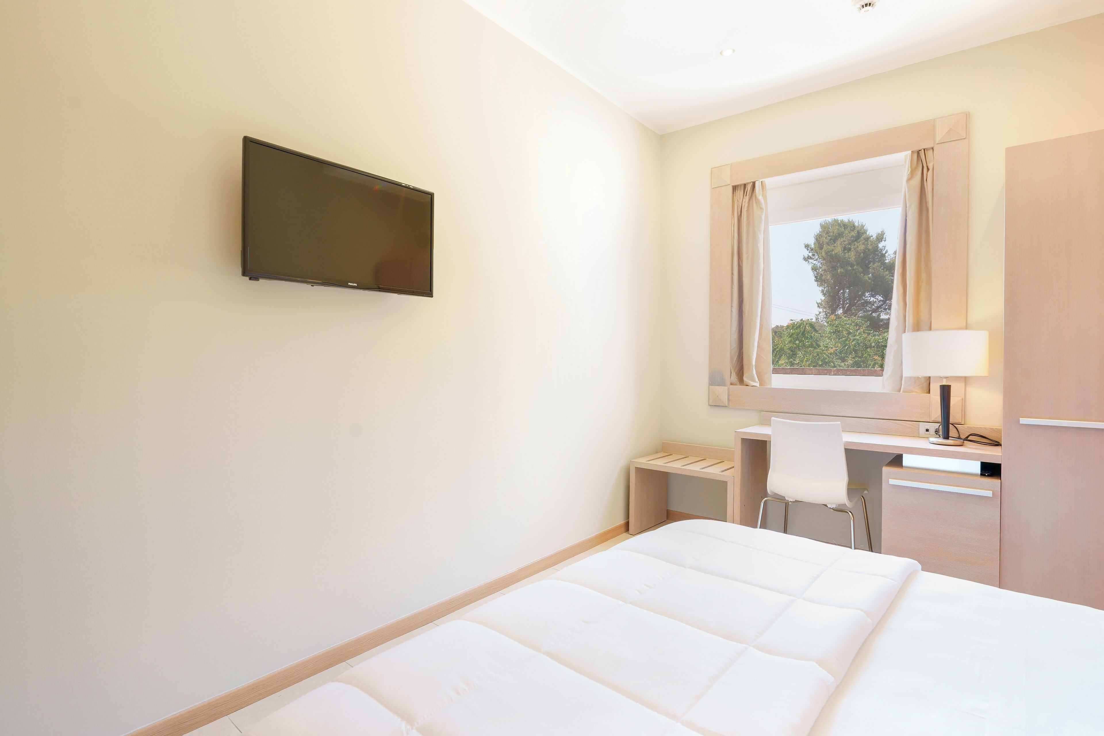 A hotel room with a bed, a desk, a chair, a TV, and a window with curtains.