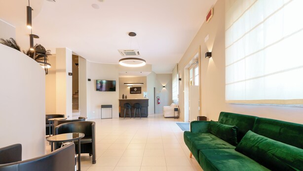 Un hall d’hôtel moderne avec un canapé vert, des chaises noires, un coin repas et une cuisine en arrière-plan.