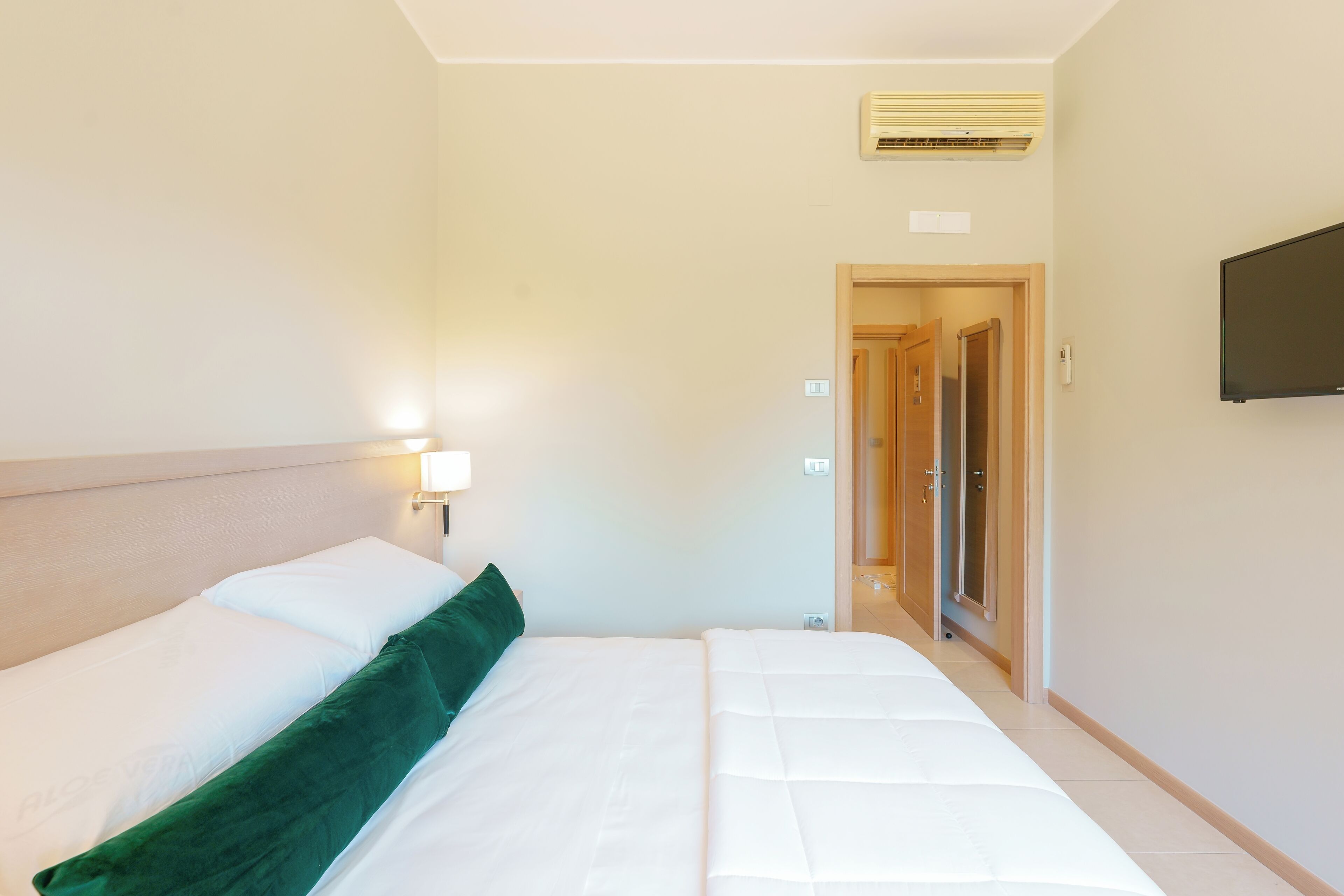 A hotel room with a bed, a TV mounted on the wall, and an air conditioning unit on the ceiling.