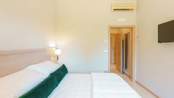 A hotel room with a bed, a TV mounted on the wall, and an air conditioning unit on the ceiling.