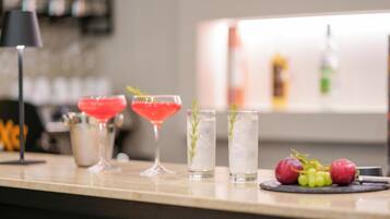 A bar area with a variety of drinks, including a red cocktail, a martini, and two tall glasses with herbs. There are also grapes and a small pitcher on the counter.