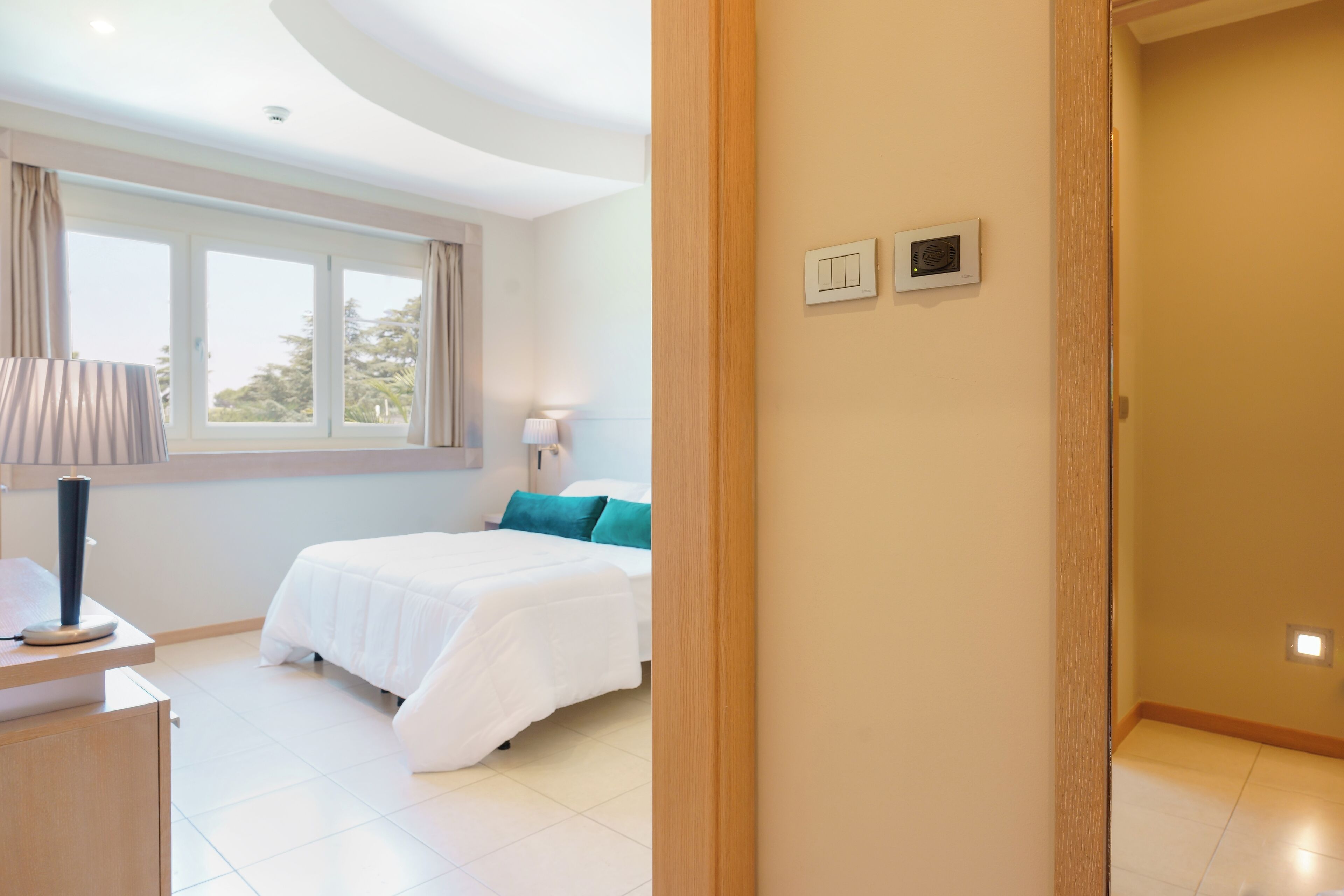 Una habitación de hotel con cama, escritorio, lámpara y ventana con cortinas.