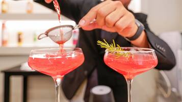 Un barman verse un cocktail rouge dans un verre à martini, en y ajoutant une branche de romarin.