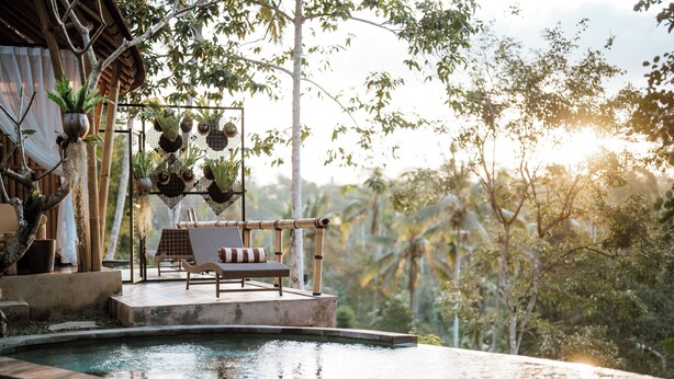 Una piscina infinita con cubierta de madera y sillones de descanso, rodeada de exuberante vegetación y una estructura de bambú.