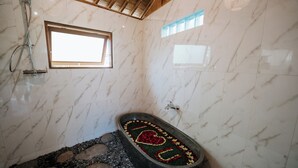 Un baño con una bañera de piedra, paredes de mármol y una ventana.