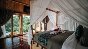 Una cama grande con dosel, suelo de madera y vistas a la vegetación exterior.