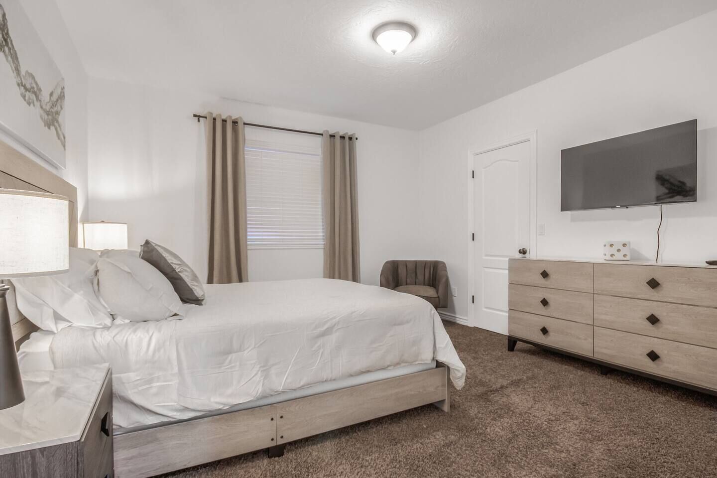 A bedroom with a bed, a dresser, a television, and a window with curtains.