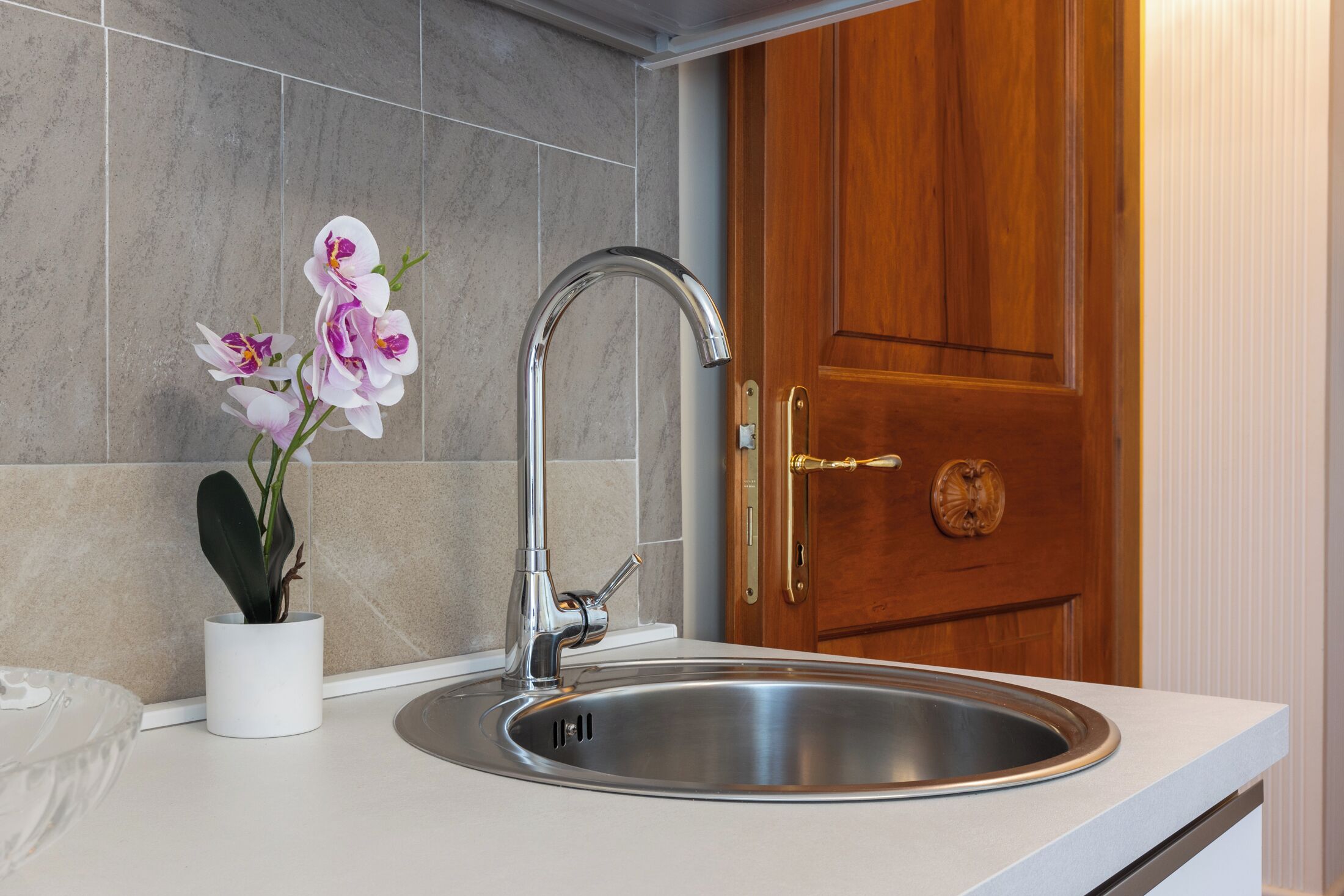 Un évier de cuisine en acier inoxydable, doté d’un robinet moderne, une orchidée en pot et une porte en bois en arrière-plan.