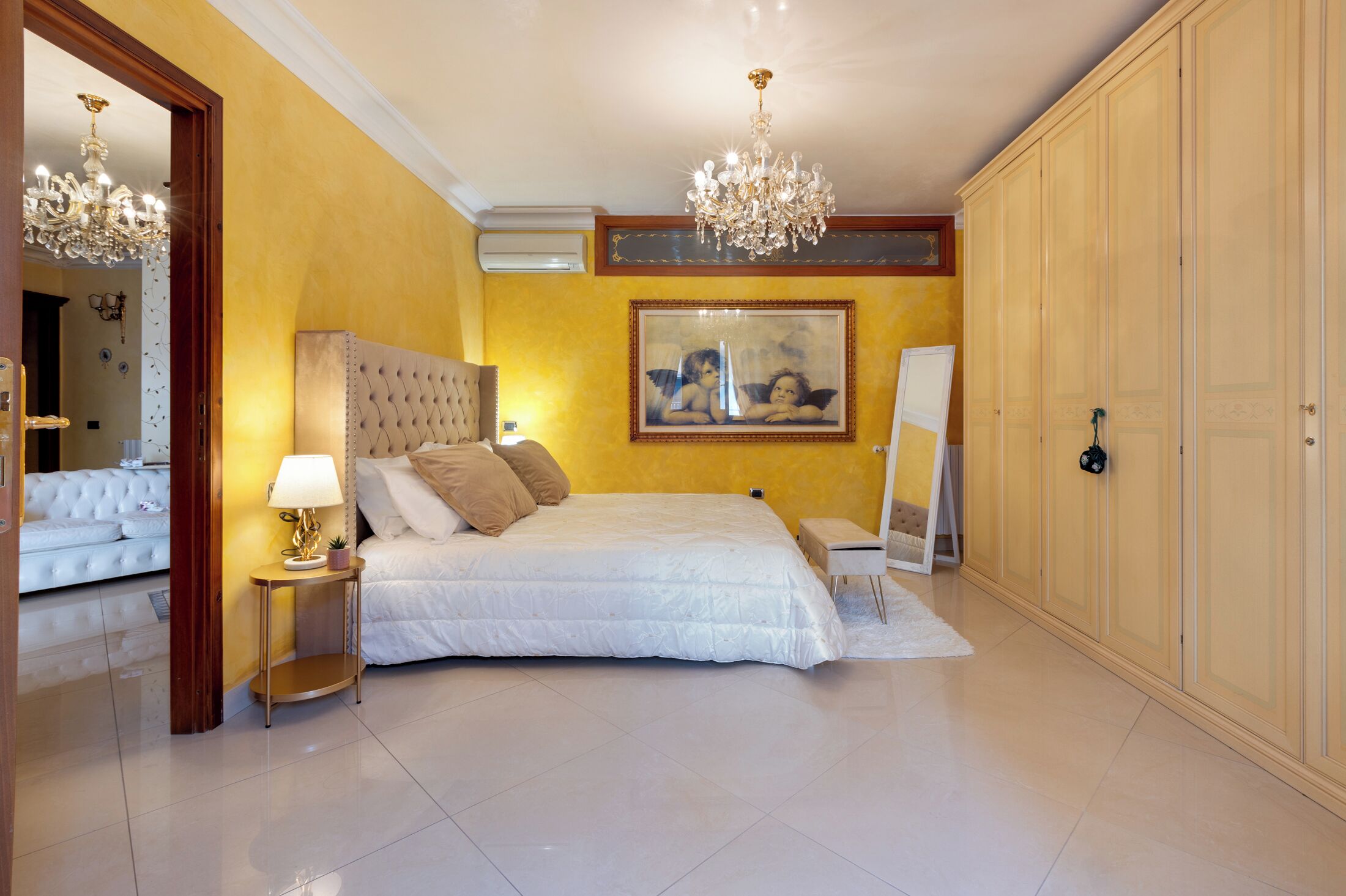 A bedroom with a large bed, a chandelier, a wardrobe, and a painting on the wall.