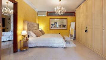 A bedroom with a large bed, a chandelier, a wardrobe, and a painting on the wall.