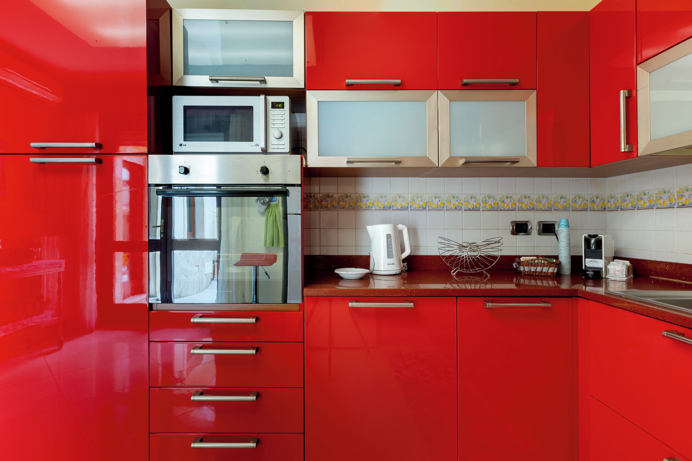A kitchen with red cabinets, a microwave, an oven, and a coffee maker.