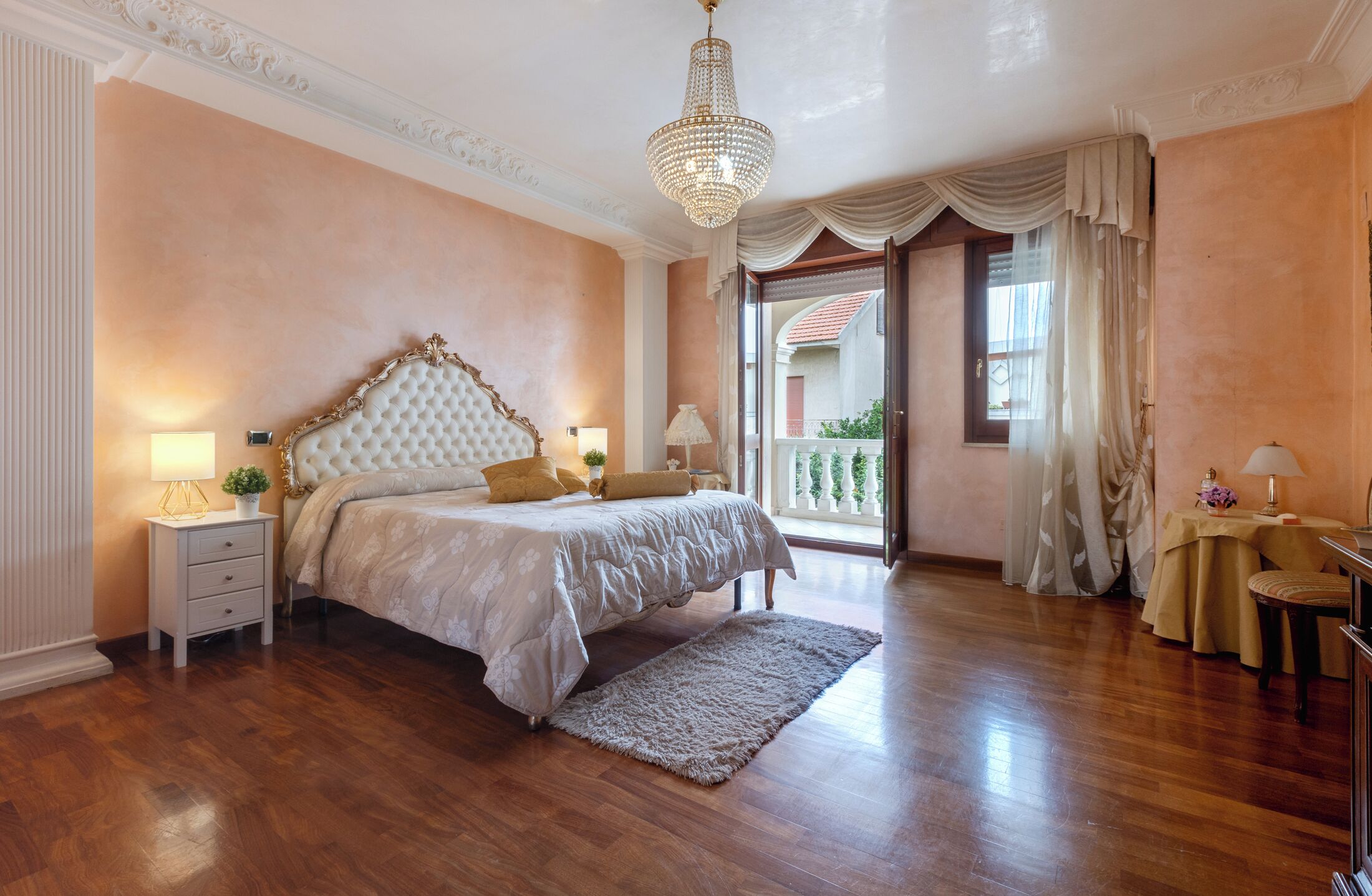 Una camera da letto con un letto grande, un lampadario, un comodino con lampada e vista sul balcone esterno.