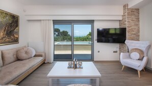 A modern living room with a sofa, armchair, coffee table, and a flat-screen TV mounted on a brick wall. - Casa Platanias Bridge (Πλατανιά)