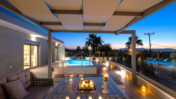 A modern outdoor seating area with a pool view, candles, and glasses. - Casa Platanias Bridge (Πλατανιά)