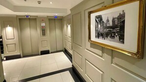 A hallway with a tiled floor, an elevator, and a framed historical photograph on the wall. - Stylish studio/ Harrods /South Kensington /Chelsea/Central London (London)