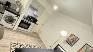 A modern bedroom with a large bed, a washing machine, and a kitchenette in the background. - Stylish studio/ Harrods /South Kensington /Chelsea/Central London (London)