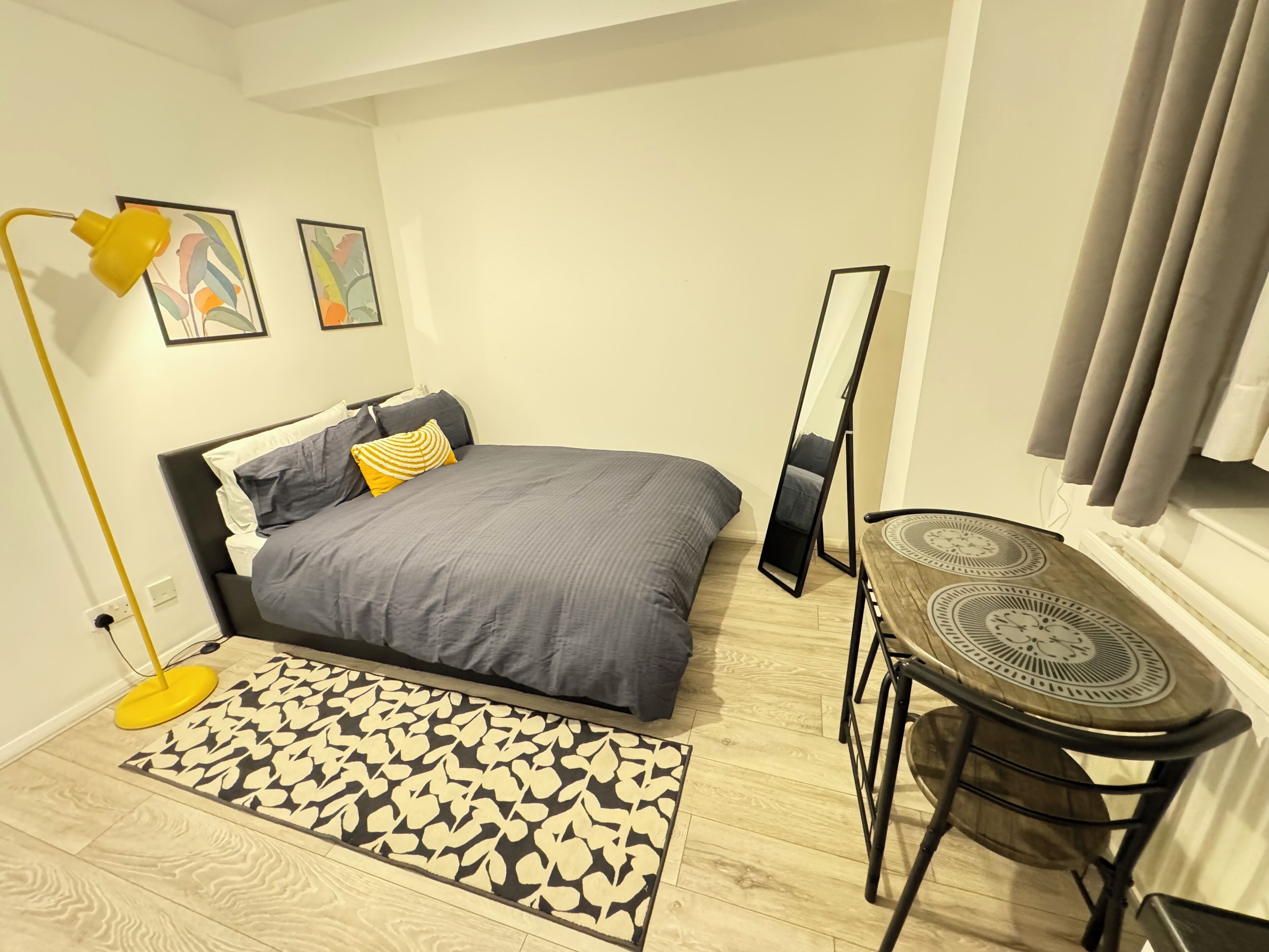 A bedroom with a bed, bedside table, chair, floor lamp, and a mirror.