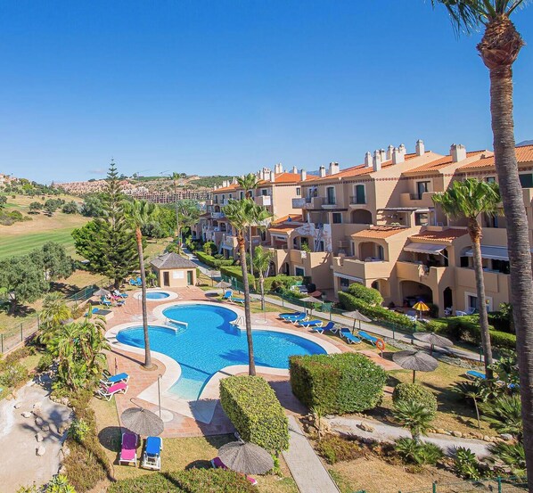 Ein Resort mit einem zentralen Schwimmbad, mehreren Balkonen und üppiger Bepflanzung.