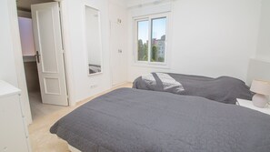 Ein Schlafzimmer mit zwei Betten, einem Fenster, einer Tür und einem Nachttisch mit Lampe.