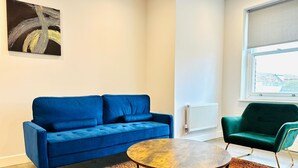 A modern living room with a blue sofa, a green armchair, and a round wooden coffee table. - Spacious 2 Bedroom Apartment in Margate (Margate)