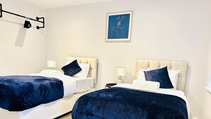 A hotel room with two beds, each with a dark blue bedspread and white linens. There is a framed artwork on the wall above the beds. - Spacious 2 Bedroom Apartment in Margate (Margate)