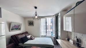 Un dormitorio pequeño con cama, un escritorio, una silla, una ventana con vistas a edificios, y una lámpara en el techo.