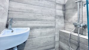 Un baño con diseño de pared de madera, un lavamanos blanco y una ducha con cabezal de ducha de mano.