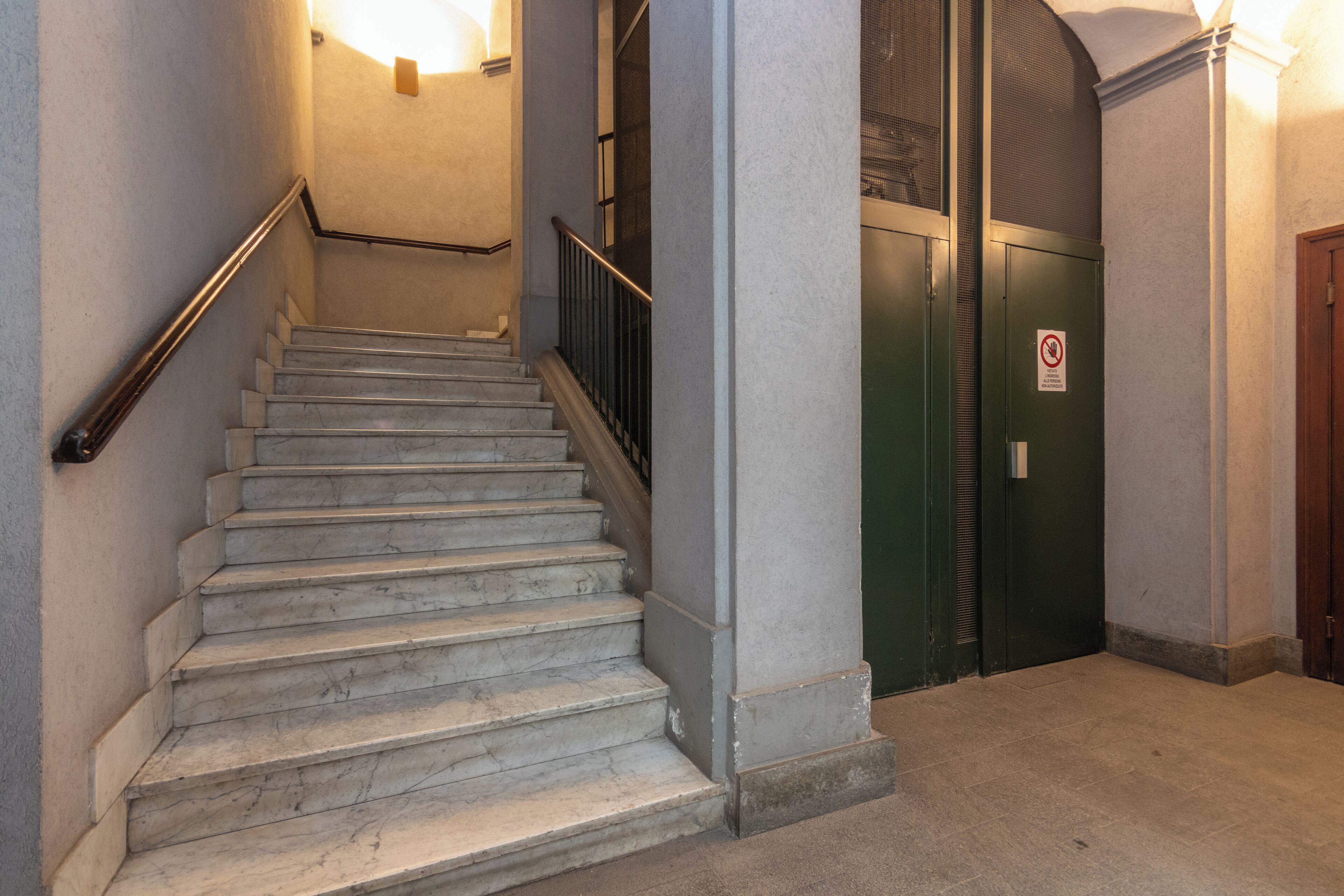 Una escalera de mármol con barandilla metálica que conduce a una puerta verde con un cartel de 'No Entrar'.