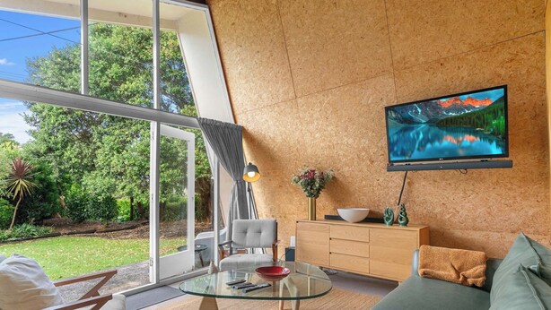 Ein modernes Wohnzimmer mit einem Glastisch, einer Couch und einem an einer Holzwand montierten Fernseher.