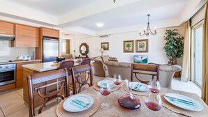 Une cuisine moderne avec des meubles en bois, un coin repas avec une table dressée pour quatre personnes, et un salon avec un canapé et une grande plante.