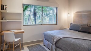 Un dormitorio con cama, escritorio y silla. Se ve una ventana con vistas a palmeras.