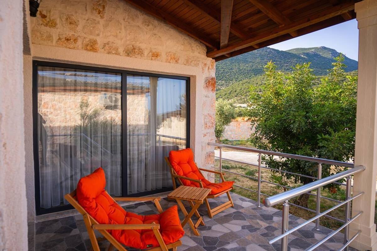 Un balcón con dos sillas de madera y una mesa, una puerta de cristal y vistas a un paisaje montañoso.