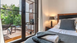A hotel room with a bed, a nightstand, a lamp, and a view of a patio with a grill and outdoor furniture. - 2 Bedrooms - Sleeps 4 - Garden and Pool With View (Benahavis)