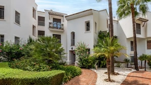 A courtyard with white buildings, palm trees, and a brick pathway. - 2 Bedrooms - Sleeps 4 - Garden and Pool With View (Benahavis)