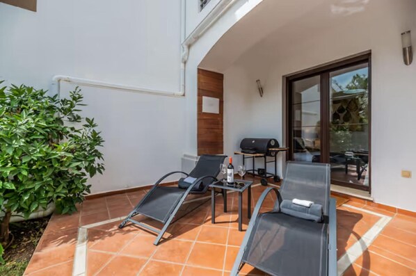Une terrasse extérieure avec deux chaises longues, une petite table et un barbecue.