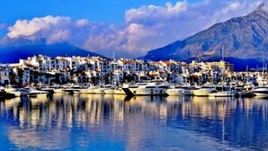 A coastal town with buildings along the waterfront, boats docked, and a mountain in the background. - 2 Bedrooms - Sleeps 4 - Garden and Pool With View (Benahavis)