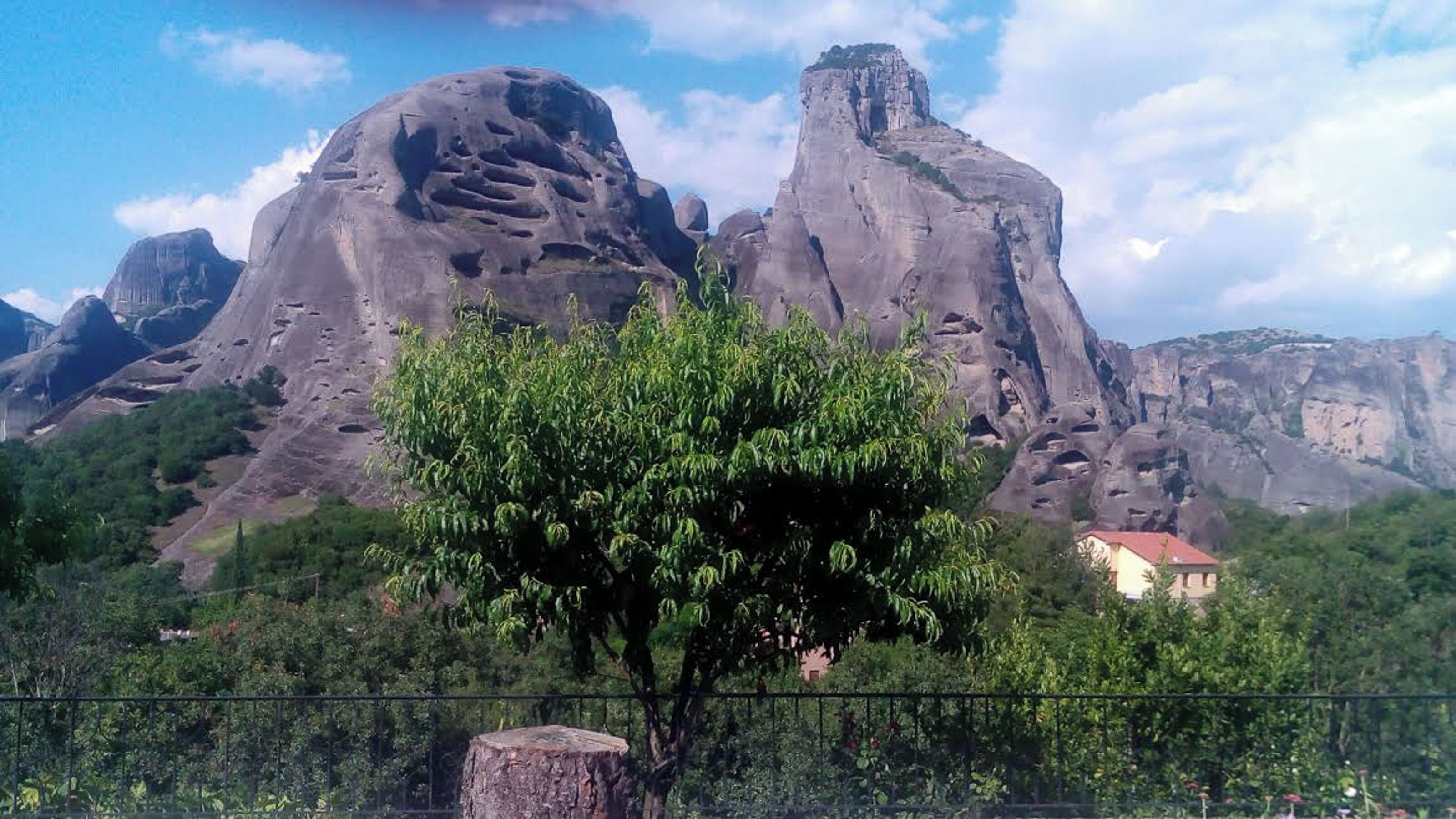 Paisaje montañoso con una formación rocosa destacada y un árbol en primer plano.