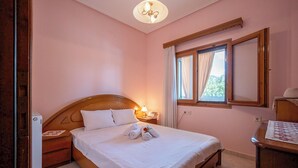A neatly made bed with white linens and towels, a bedside table with a lamp, a window with curtains, and a wooden headboard. - Majestic view Home just under Meteora Unesco Site

 (PJ57+9V6 Kalabaka)