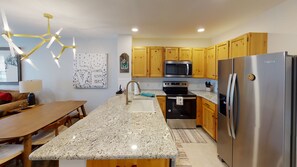 A modern kitchen with granite countertops, stainless steel appliances, wooden cabinets, and a pendant light fixture.